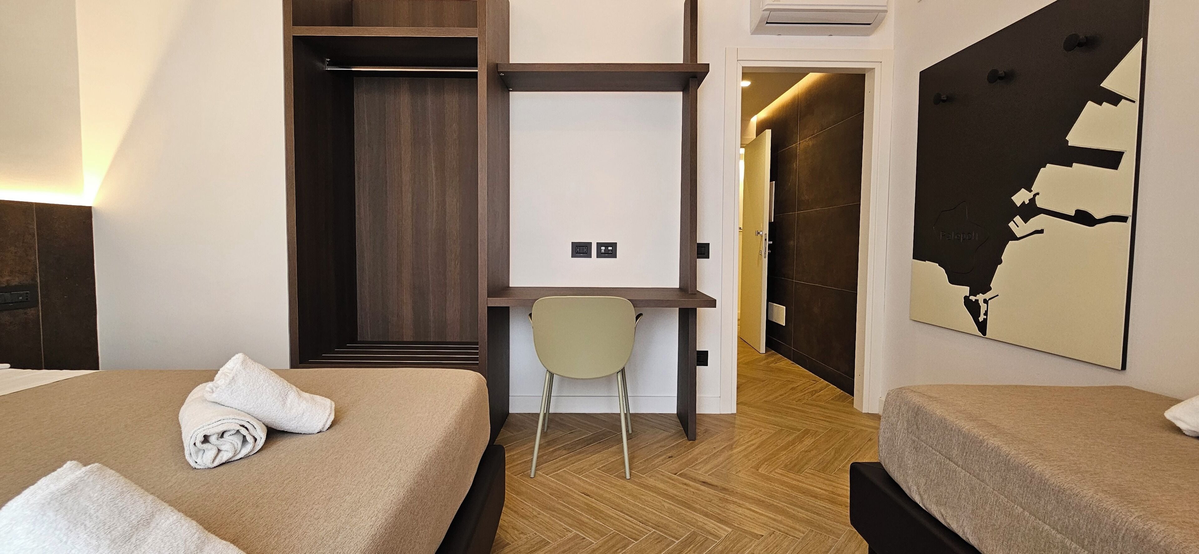 A hotel room with two beds, a desk, a chair, a map on the wall, and a wardrobe.