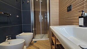 Un bany modern amb plat de dutxa envoltat de vidre, un vàter blanc i un bidet.