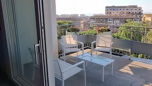 Un balcon doté d’une porte vitrée donnant sur un espace extérieur aménagé avec des chaises blanches et une table.