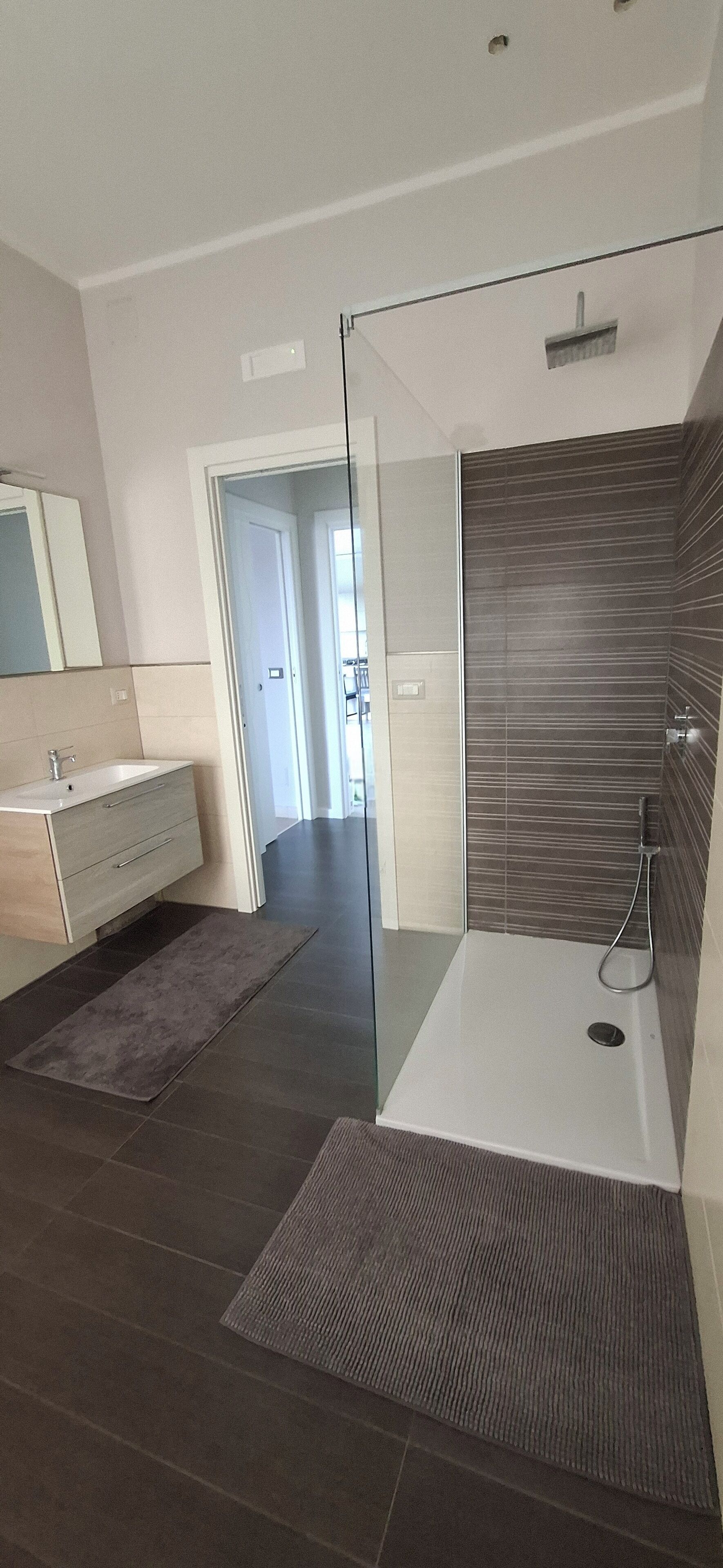 A modern bathroom with a glass shower enclosure, a separate sink area, and a dark tiled floor.