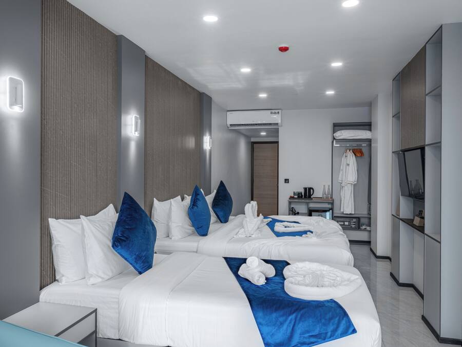 A modern hotel room with a large bed, a bedside table, a wardrobe, and a bathroom visible in the background.