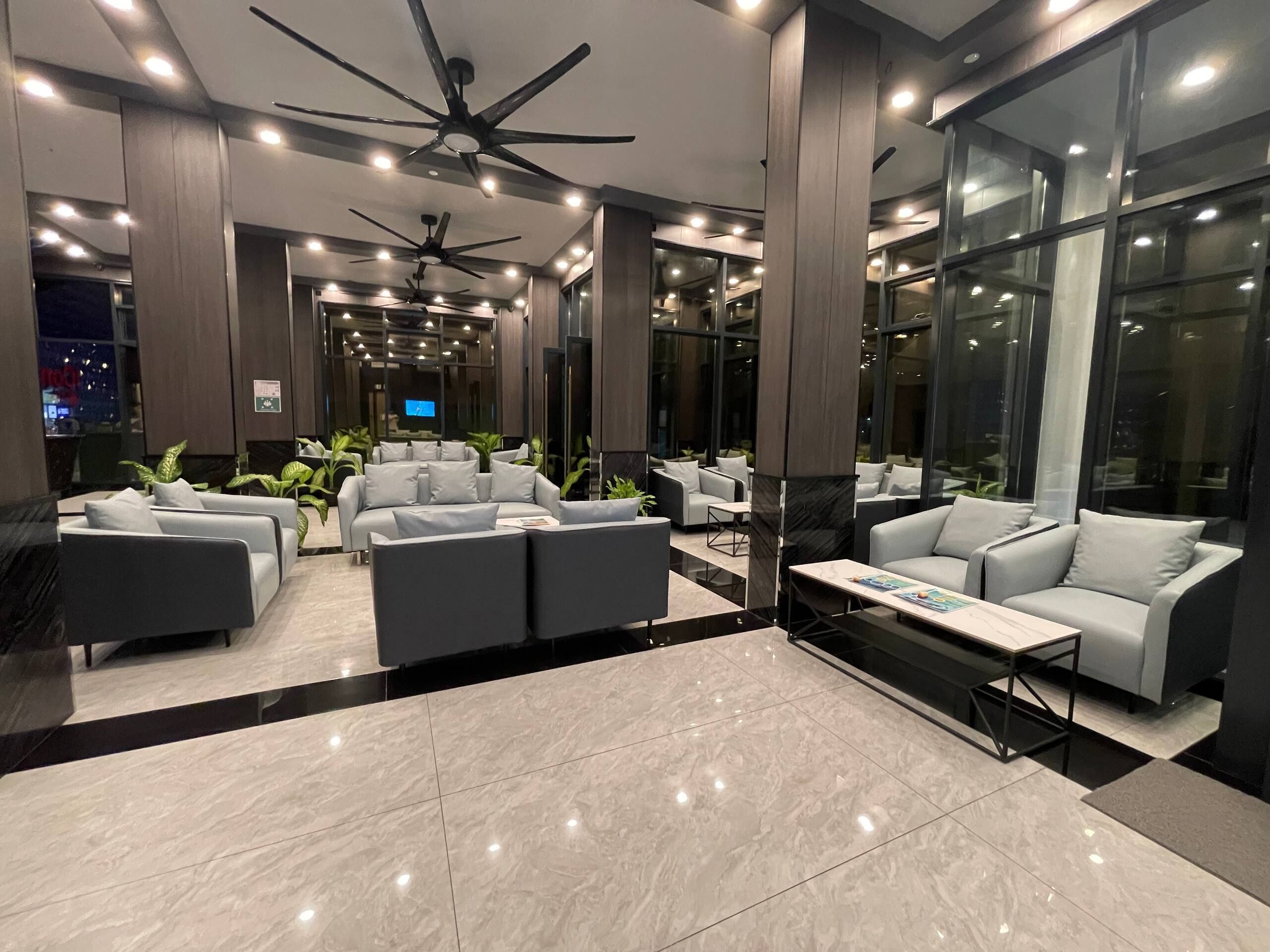 Eine moderne Lobby mit grauen Sofas, einem Couchtisch und einem Deckenventilator.