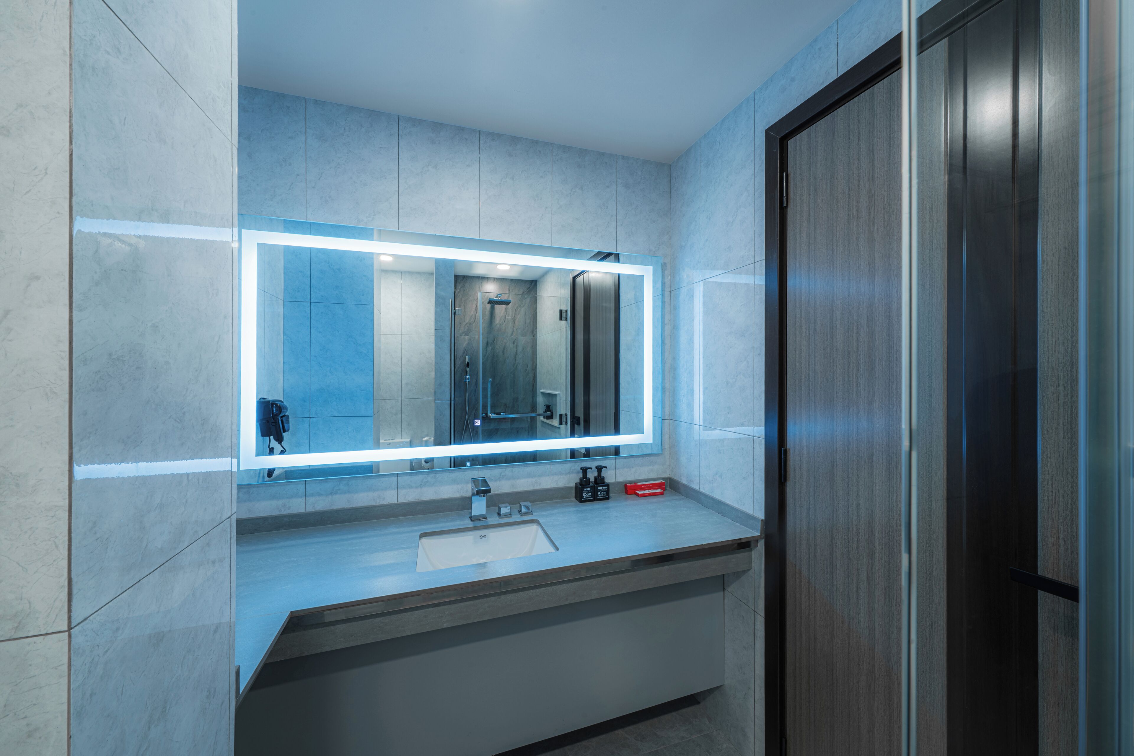 A modern bathroom with a large mirror, a sink, and a shower.