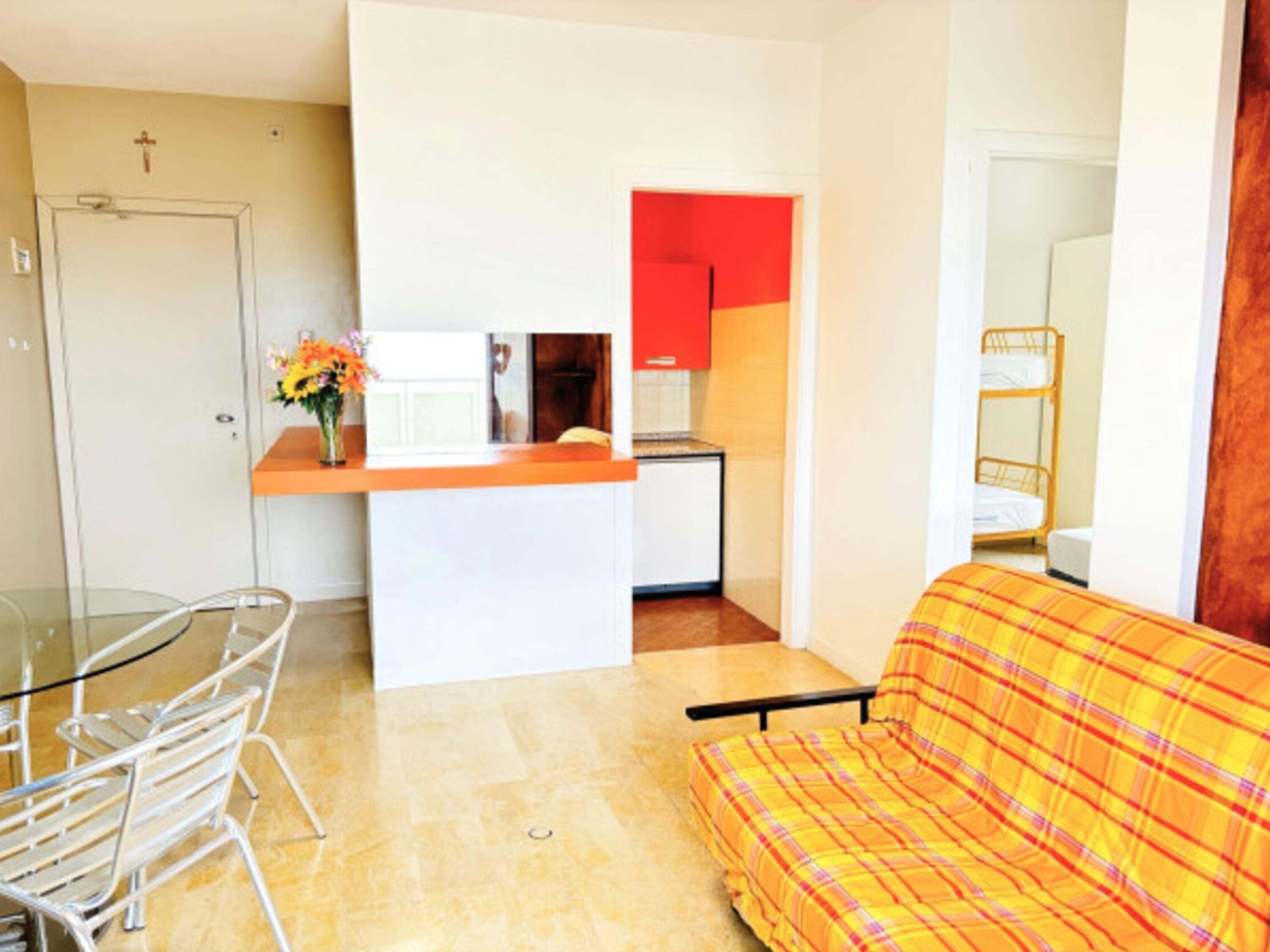 A compact living space with a kitchenette, a dining area with a glass table, and a sofa.