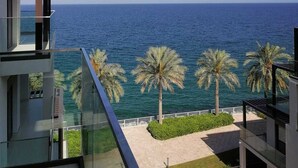 A modern building with a glass balcony overlooking a beach with palm trees and the sea.