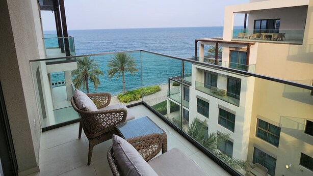 A balcony with wicker furniture, a glass railing, and a view of the sea.