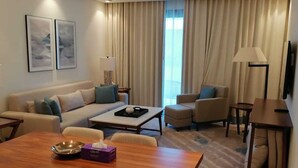 A modern hotel room with a living area, a dining table, and a sofa.
