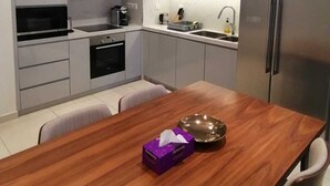 A modern kitchen with grey cabinets, a wooden dining table, and a stainless steel refrigerator.