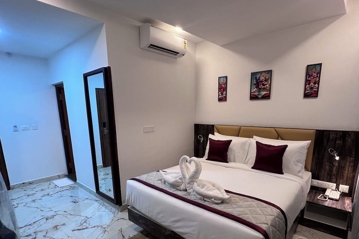 Habitació d'hotel amb llit, taulell de nit, aparell d'aire condicionat i una porta.