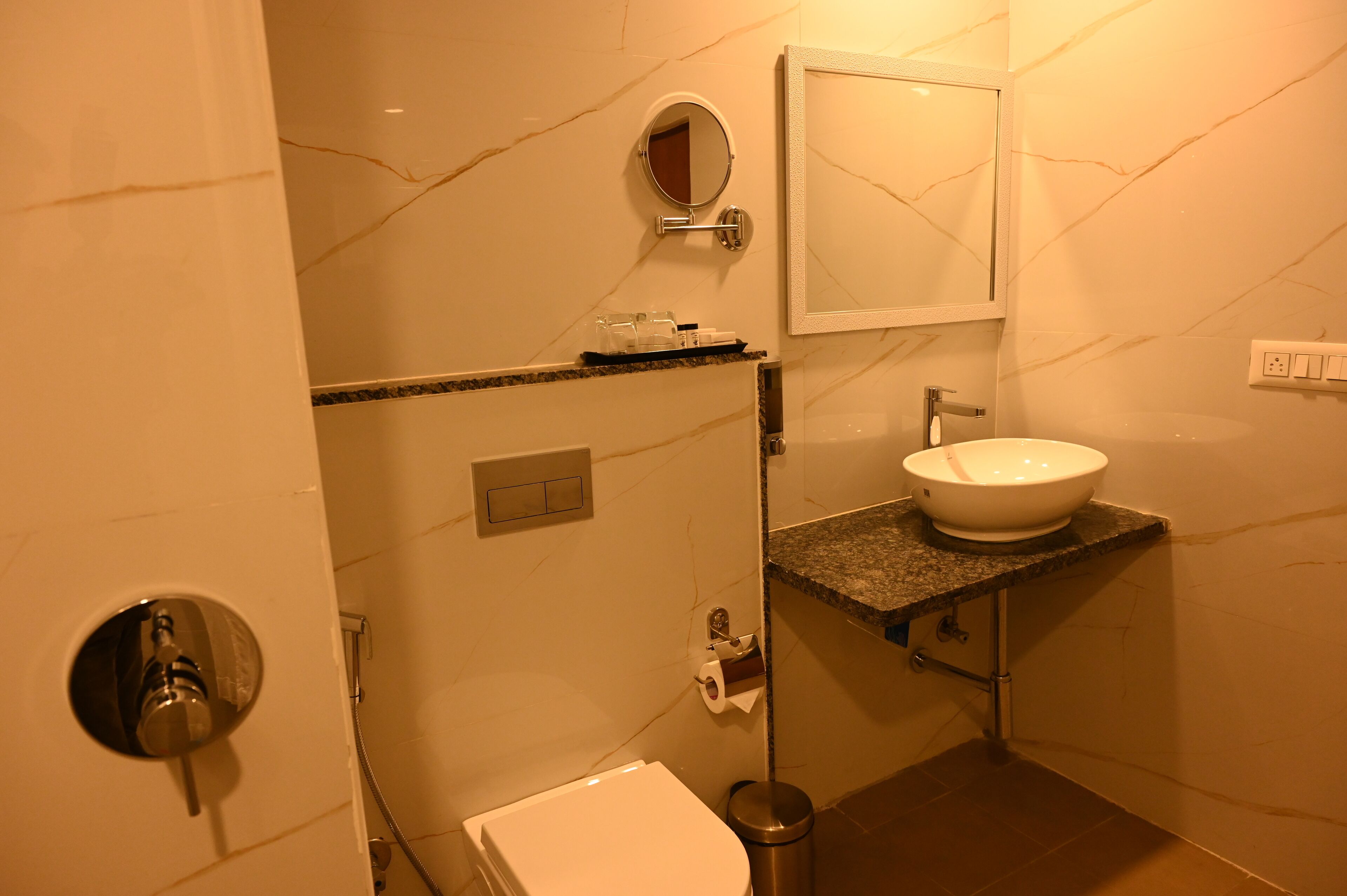 A bathroom with a marble wall, a sink, a toilet, a mirror, and a towel rack.