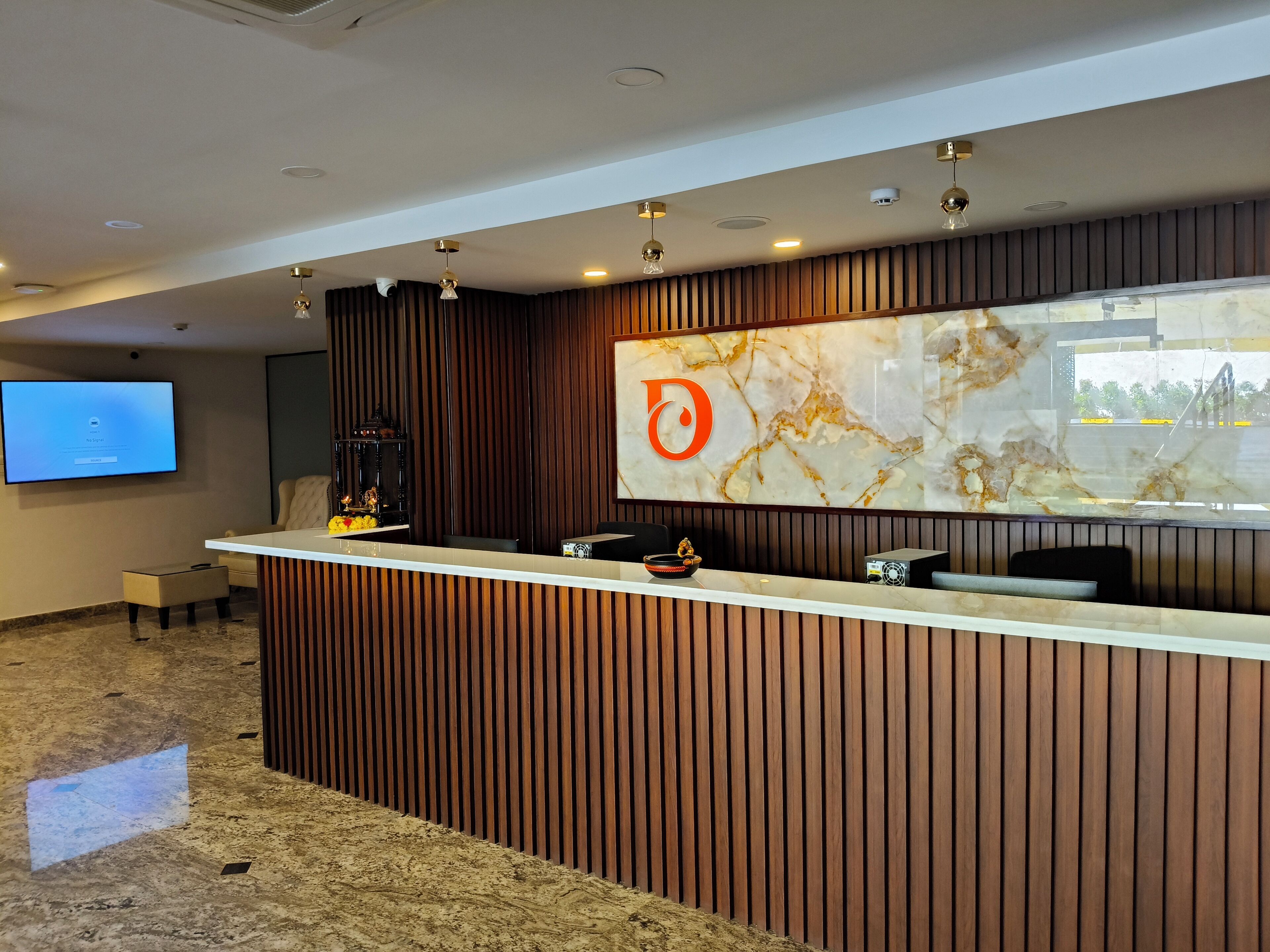 A modern reception desk with a marble accent wall, a mounted TV, and a logo.