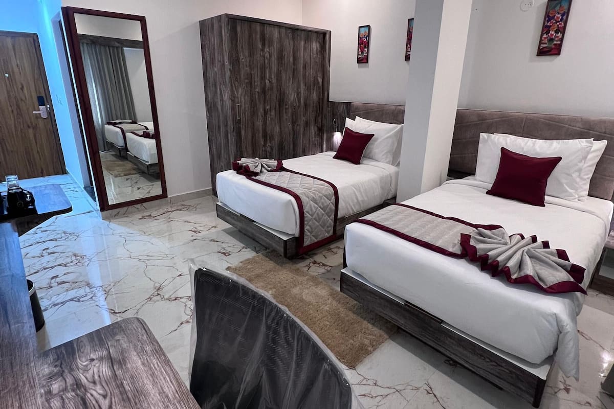 Habitació d'hotel amb dos llits, un armari de fusta, un sòl de marbre, un escriptori de fusta i un mirall.