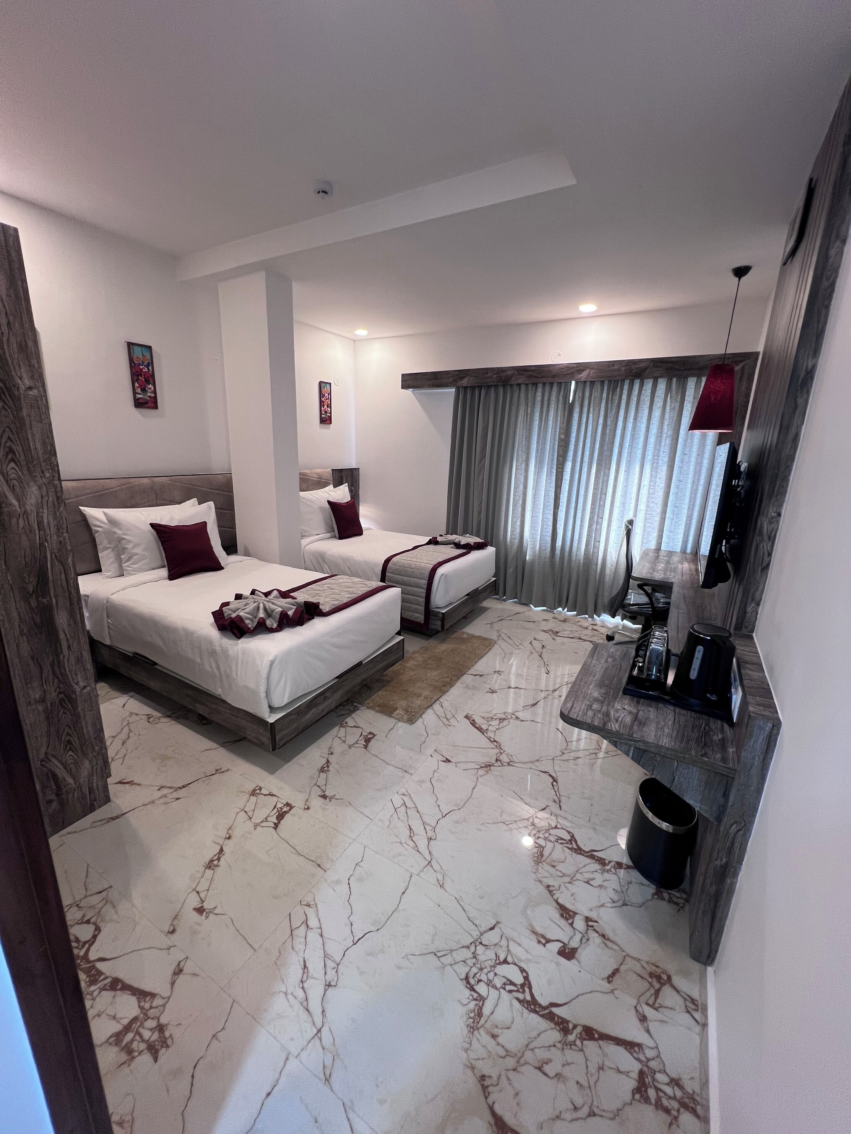 A modern hotel room with a marble floor, two beds with white linens, a coffee machine, and a TV on a wooden shelf.