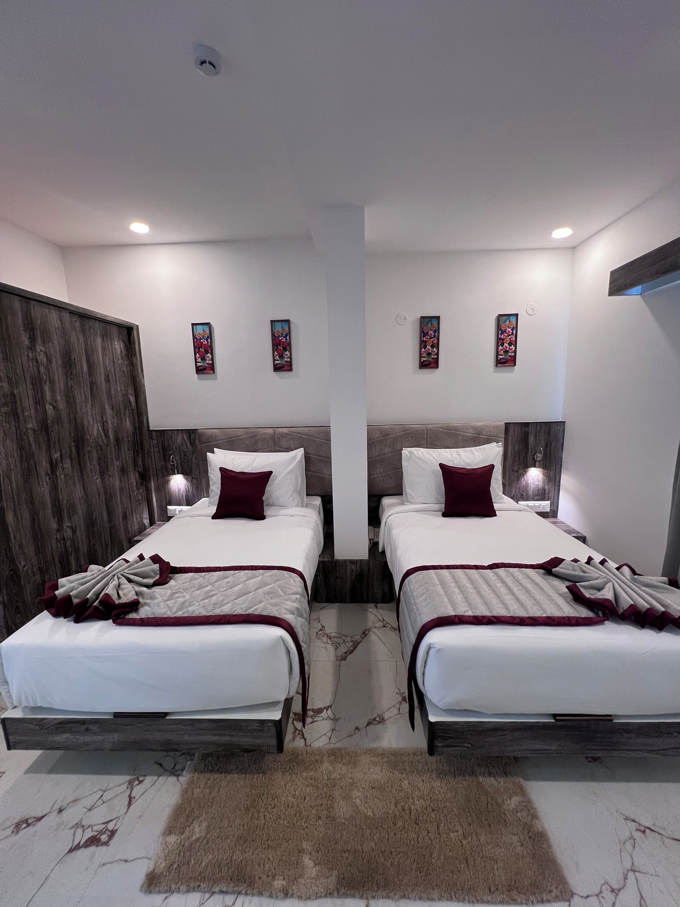 Habitación de hotel con dos camas, cabecero de madera, suelo de mármol y dos obras de arte colgadas en la pared.