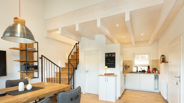 A modern kitchen with white cabinets, a wooden dining table, and a staircase leading to another level.