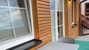A wooden exterior wall with a window, a door, and a small outdoor seating area with a table and chairs.
