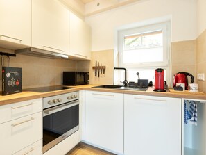 A modern kitchen with a microwave, stove, sink, and red coffee maker.