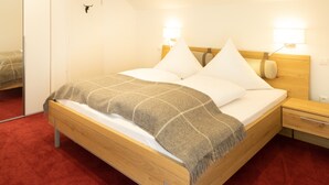 A neatly made bed with a headboard, two bedside lamps, a wooden nightstand, and a red carpeted floor.