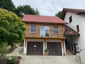 A two-story house with a red-tiled roof, two garage doors, a balcony, and a stone staircase leading to the entrance.