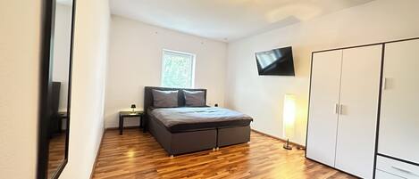 A bedroom with a bed, a TV, a wardrobe, and a window.