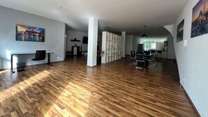 A spacious living area with a wooden floor, a desk with a chair, a TV mounted on the wall, and a dining area with chairs and a table. - Luxury loft in Bayreuth Central&Exclusiv (Bayreuth)