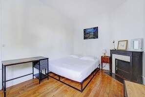 Quarto com cama, escrivaninha, cômoda, lareira e um quadro na parede.