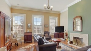 Un salon comprenant un canapé, des fauteuils, un téléviseur, une cheminée et de grandes fenêtres.