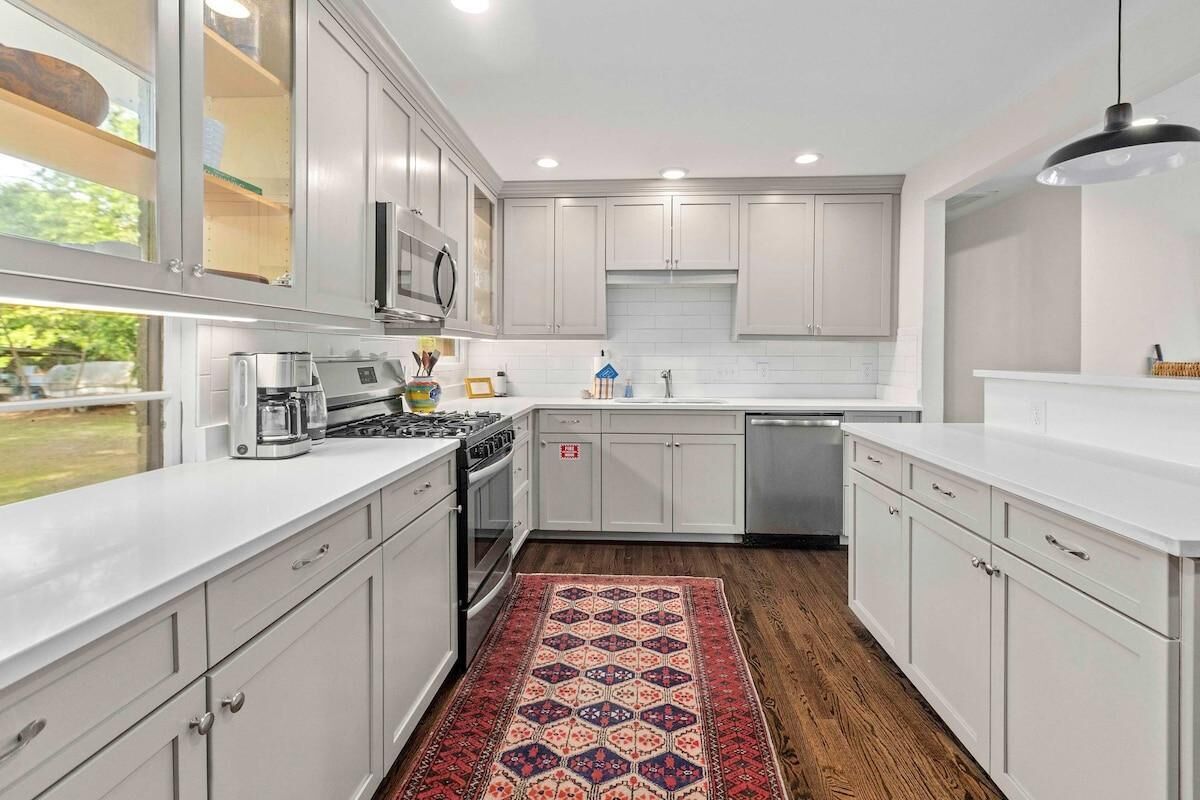 A modern kitchen with white cabinets, stainless steel appliances, and a patterned rug.