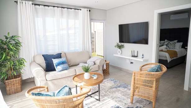 A modern living room with a sofa, two wicker chairs, a coffee table, and a TV mounted on the wall. - Cosy Private Cottages- 3 bedrooms, pool and dstv  (Durban North)