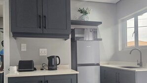 A modern kitchen with grey cabinets, a stainless steel refrigerator, a kettle, and a window with a view. - Cosy Private Cottages- 3 bedrooms, pool and dstv  (Durban North)