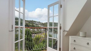 A room with a wooden balcony, white walls, and a view of a hillside town.