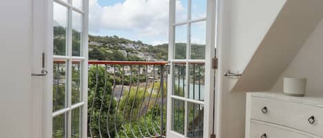 A room with a wooden balcony, white walls, and a view of a hillside town.