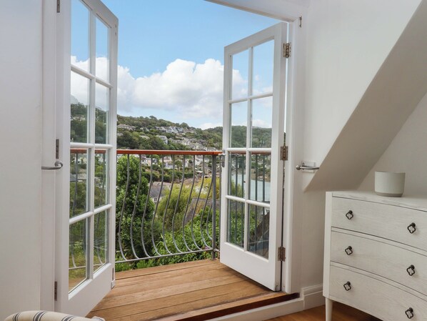 A room with a wooden balcony, white walls, and a view of a hillside town.