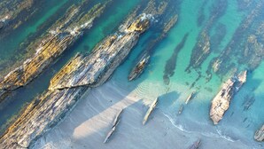 An aerial view of a coastal area with large rock formations and clear turquoise waters.
