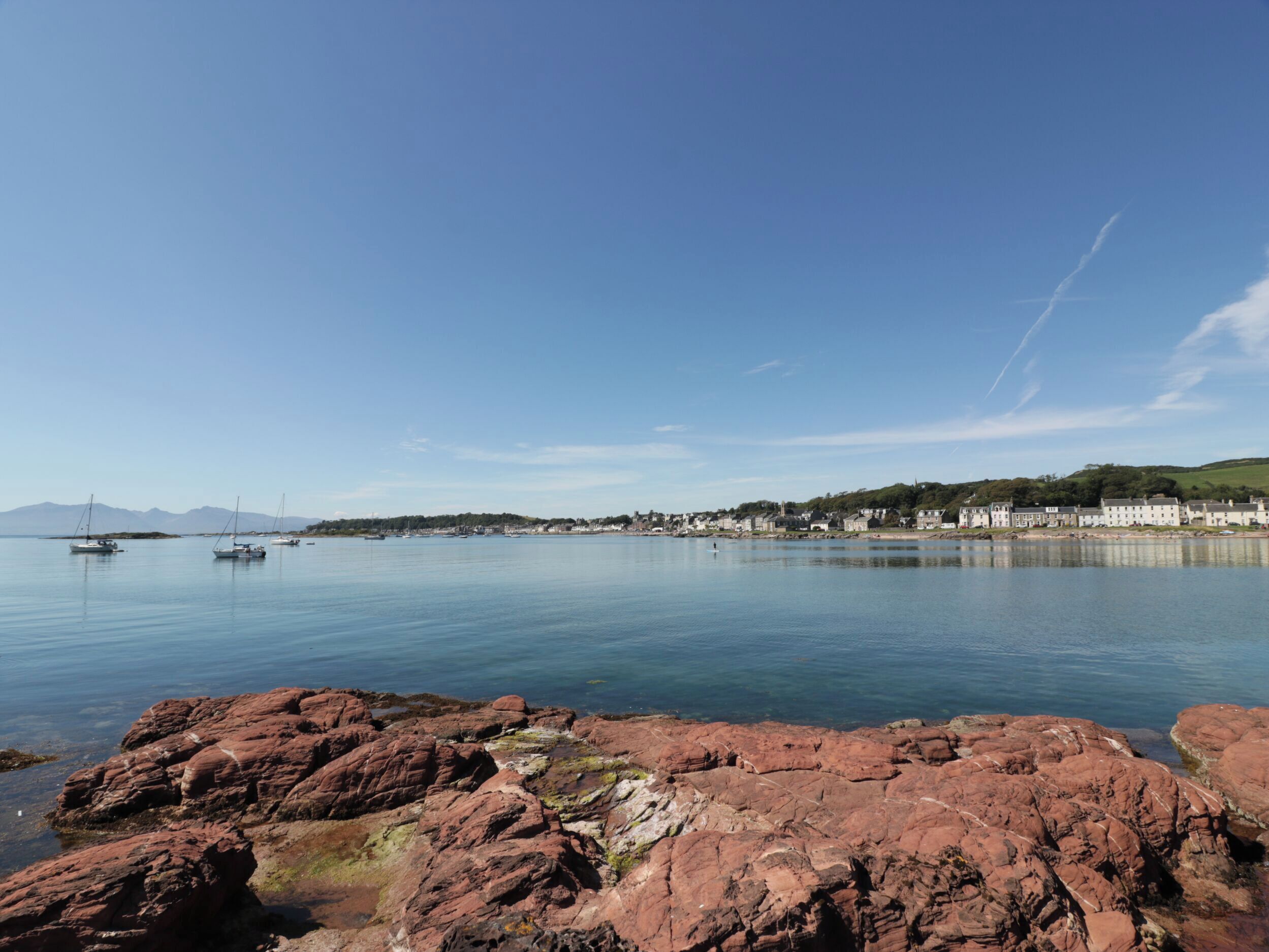 A coastal town with calm waters, rocky shoreline, and buildings along the coast.
