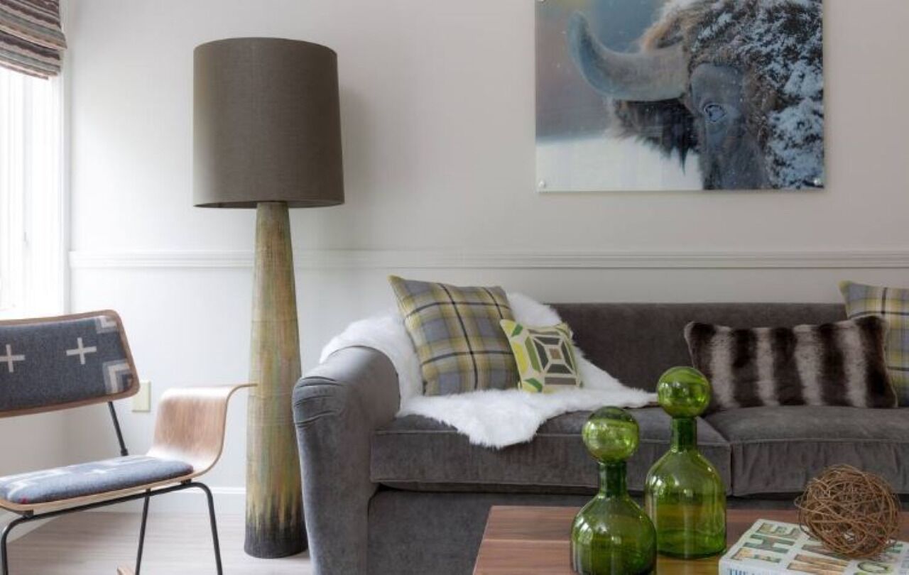 Een woonkamer met een grijze bank, een witte vacht en groene vazen op een houten salontafel.