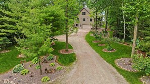 A house with a gravel driveway leading to a garage, surrounded by a well-maintained garden with various plants and trees. - Private beach house in charming Pound on a clear, sandy full rec lake (Pound)
