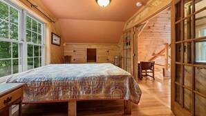 A cozy log cabin bedroom with a large bed, wooden walls, and a window overlooking greenery. - Private beach house in charming Pound on a clear, sandy full rec lake (Pound)