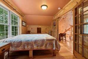 Un dormitorio acogedor tipo cabaña de madera con una cama grande, paredes de madera y una ventana con vistas a la vegetación.