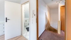 Een kamer met een houten deur, een witte muur, een klein raam en een witte radiator.
