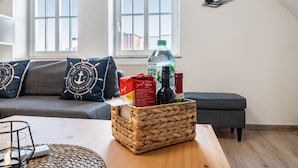 Een woonkamer met een bank, een bijzettafeltje, een rieten mand en een raam met uitzicht.
