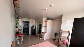 Un dormitorio con cama, escritorio, silla, armario y ventilador.