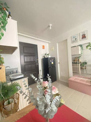 A compact kitchen with a refrigerator, a microwave, and a sink. There are potted plants and a dining area with a red table runner. - Studio type Condo in Plumera, Lapu-Lapu City, Cebu, Philippines (Lapu-Lapu)