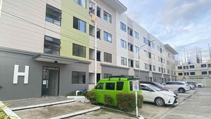 Un hotel de varios pisos con diseño moderno, que cuenta con un estacionamiento y varios coches, además de una furgoneta verde.