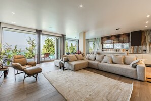 A modern living room with a large sectional sofa, a leather armchair, and a large window offering a view of greenery and mountains. - Lake Whisper Villa Pool Amazing Views (Shkodër)