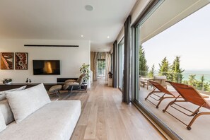A modern living room with a sofa, TV, and a balcony with outdoor seating. - Lake Whisper Villa Pool Amazing Views (Shkodër)