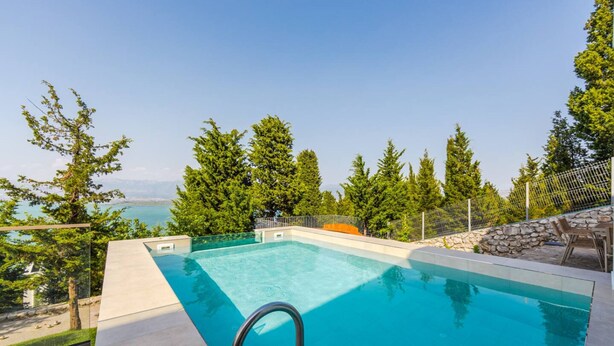 Una piscina rectangular con agua azul cristalina, rodeada por un muro de piedra y una barandilla metálica.