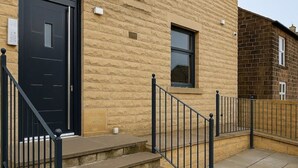 A building with a black door, a window, and a set of stone steps leading to a black metal railing. - Westview Luxe Apartment (Newsome)