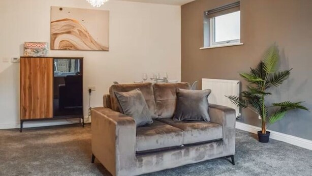 A living room with a grey sofa, a wooden cabinet, a chandelier, a radiator, and a window. - Westview Luxe Apartment (Newsome)