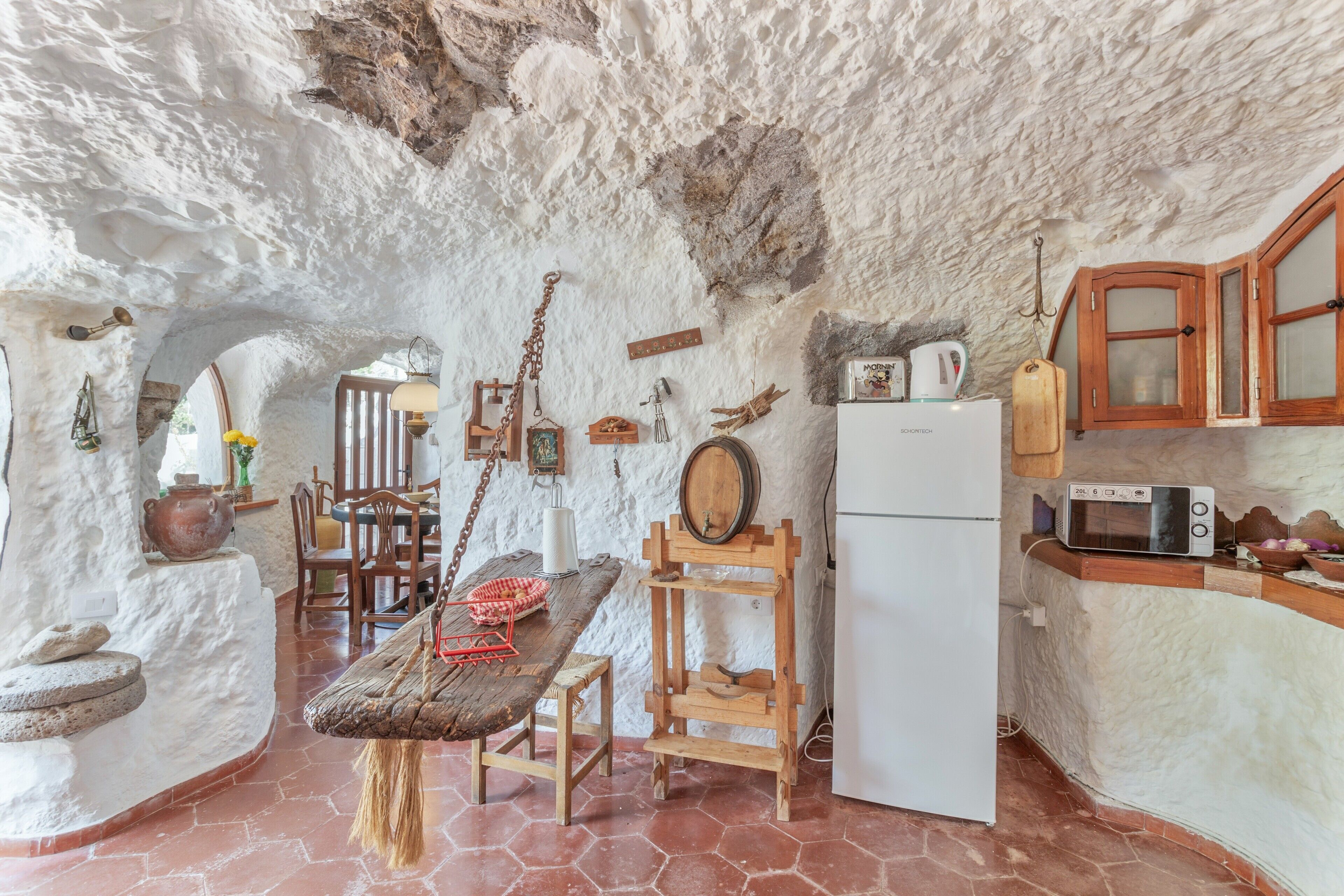 Una cocina rústica con paredes de piedra, una mesa de madera y un refrigerador blanco.